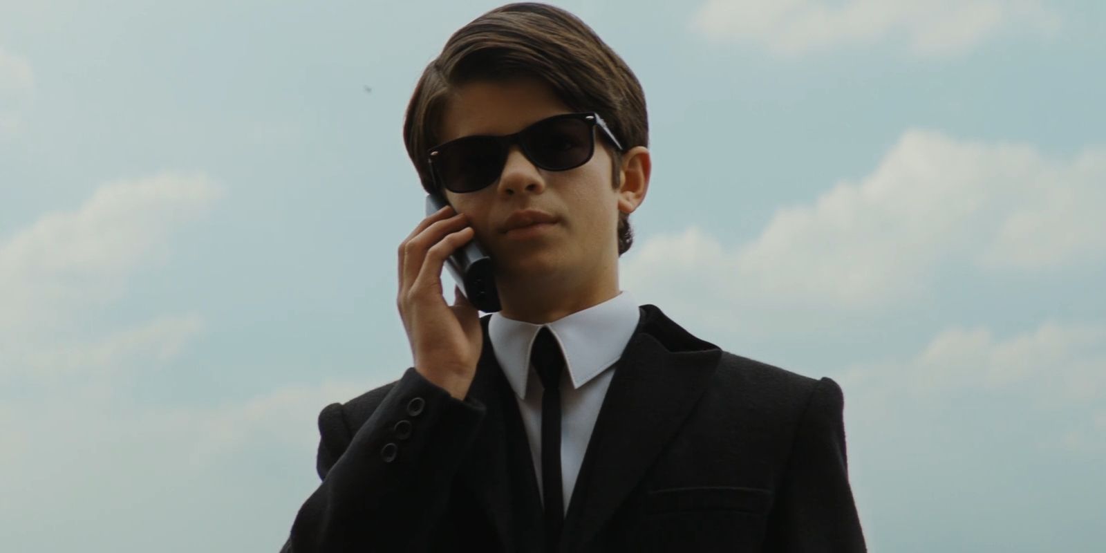 Artemis Fowl, played by Ferdia Shaw, holds a phone to his ear while wearing sunglasses in 'Artemis Fowl'.