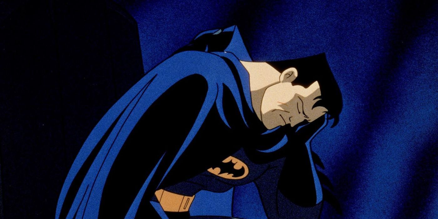 Batman sits with his head in his hand and his mask off, looking sad in Batman: Mask of the Phantasm.