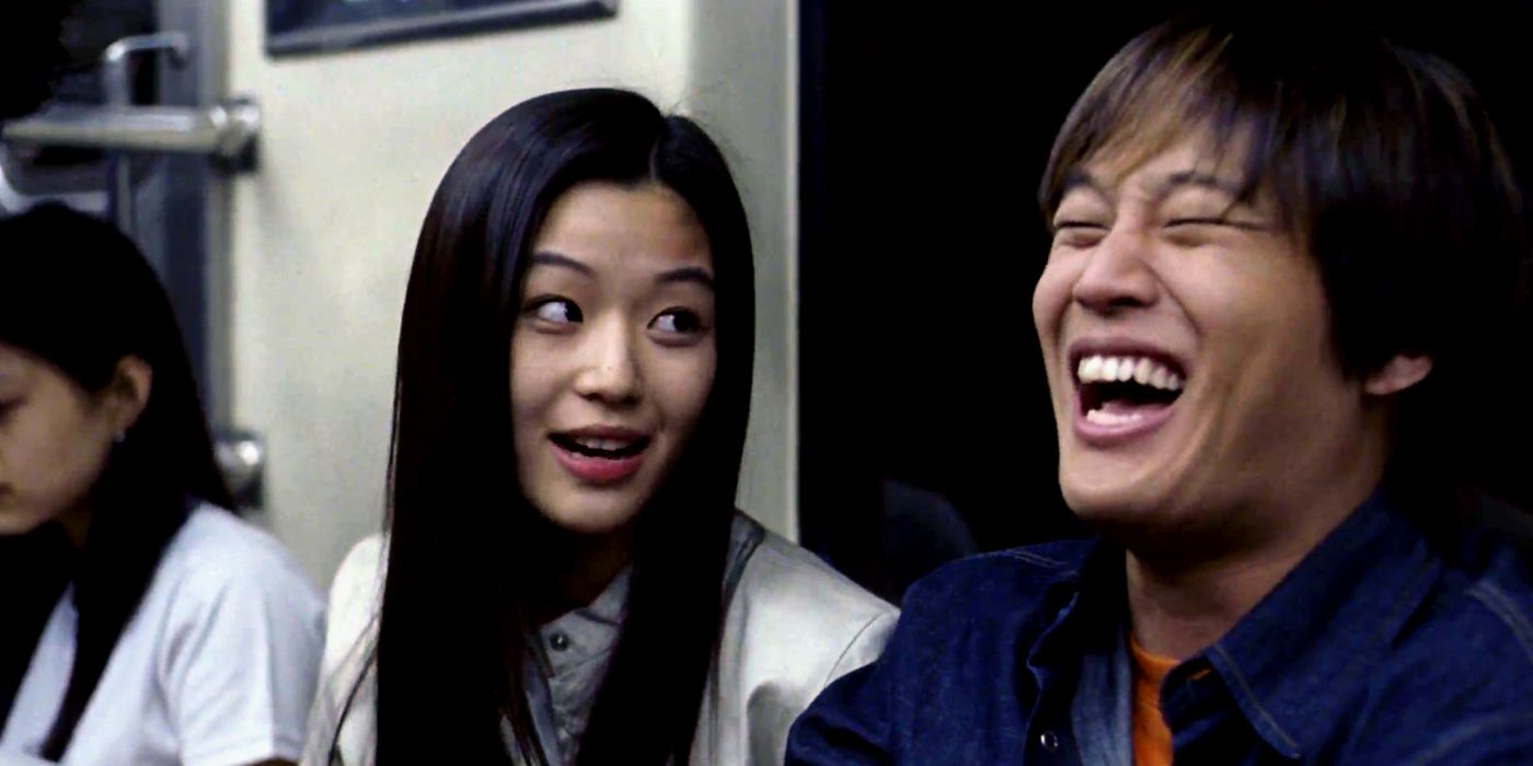 A girl talking to a man in a subway, making him laugh out loud, judging by his wide open smile