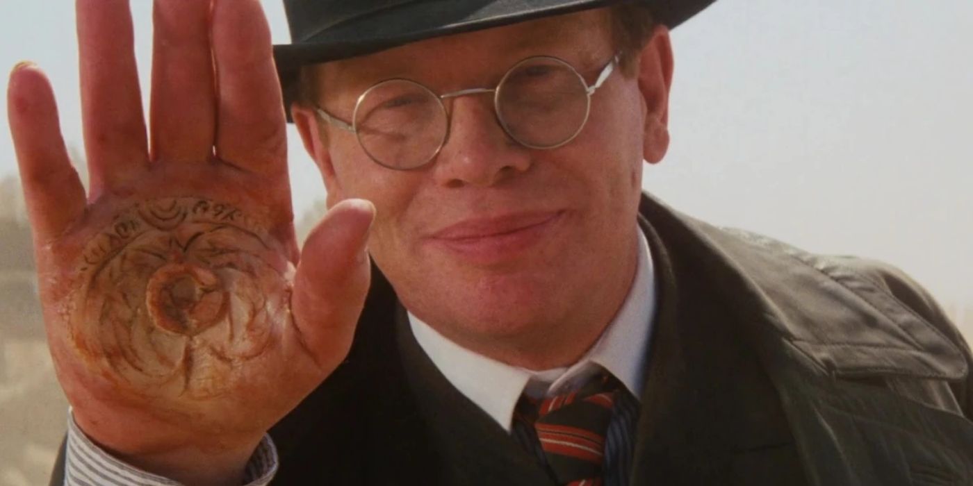 Ernst Toht smiling and raising his open palm in Raiders of the Lost Ark