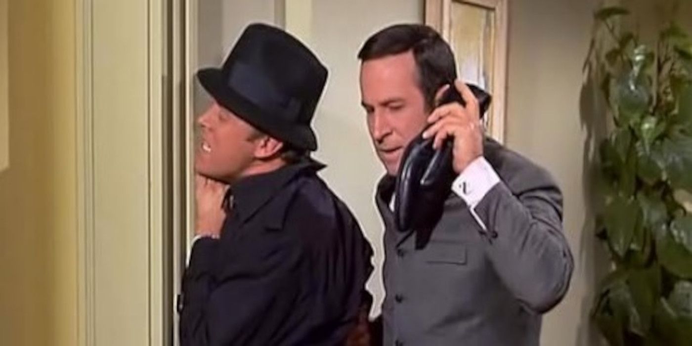 Maxwell Smart talks into his shoe phone while apprehending a suspect in Get Smart.