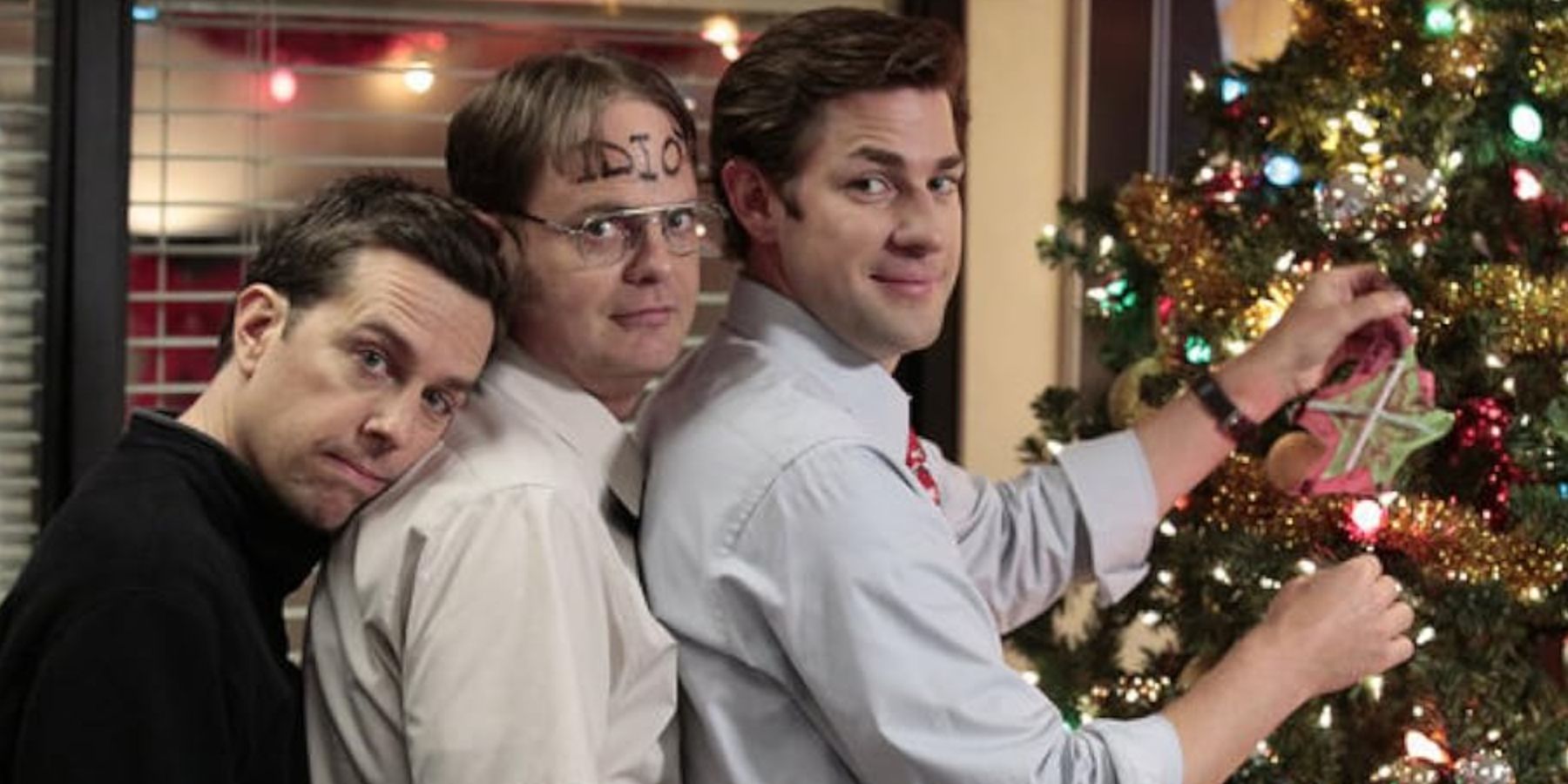 Andy (Ed Helms), Dwight (Rainn Wilson) and Jim (John Krasinski) standing near a Christmas tree in the office.