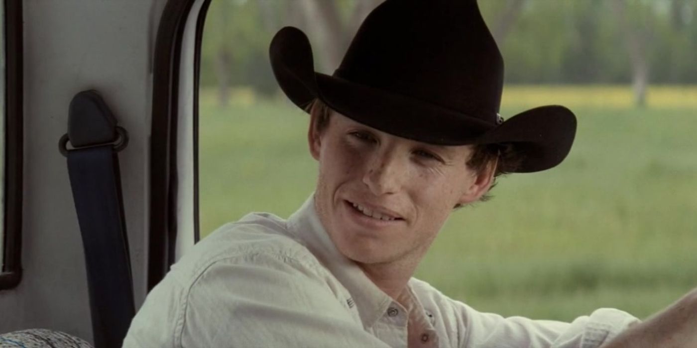 Eddie Redmayne as Eddie in Hick, wearing a white shirt and a black cowboy hat, smiling at someone in the passenger&rsquo;s seat