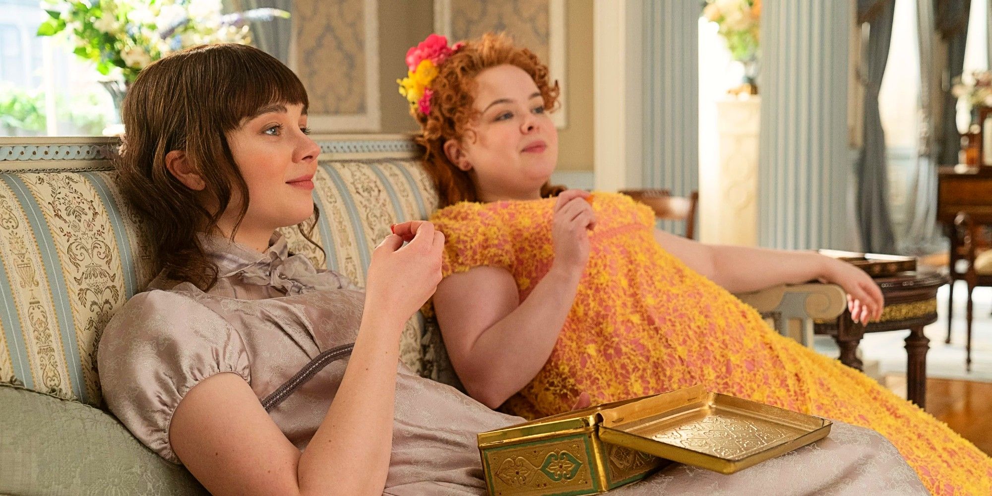 Eloise and Penelope eating chocolates on a couch in Bridgerton.