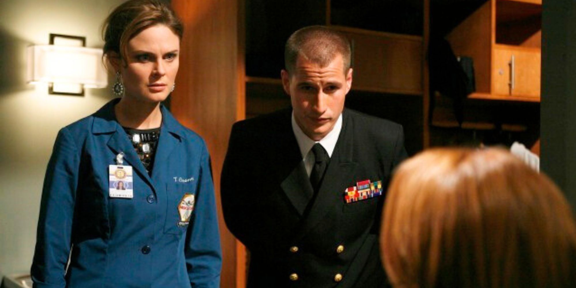 Emily Deschanel standing next to Brendan Fehr both looking at someone who has their back to the camera in Bones episode The Hero in the Hold