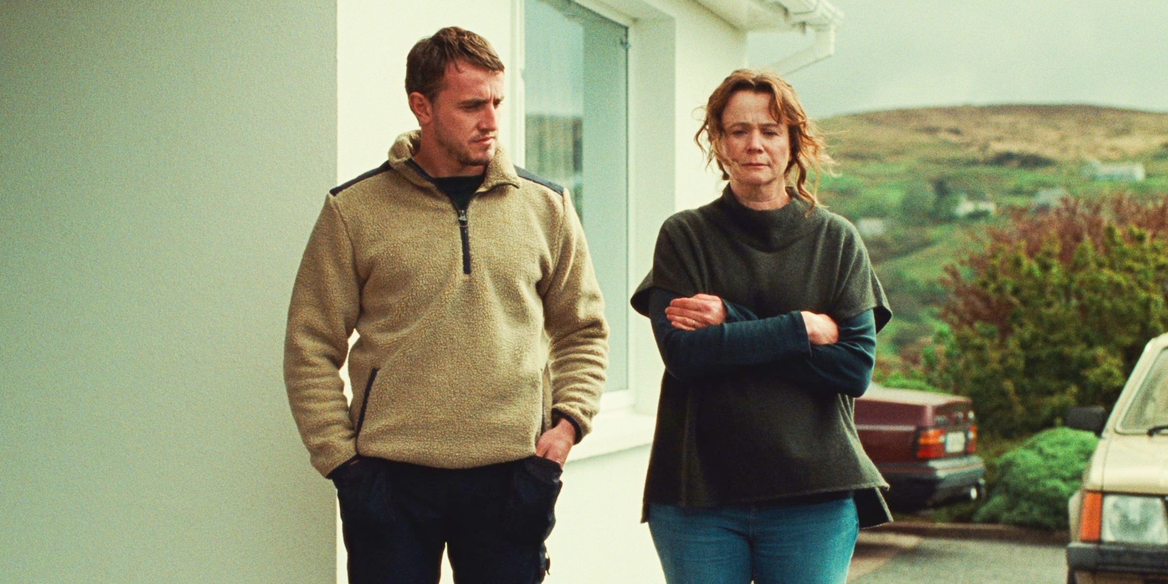 Aileen and Brian, played by actors Emily Watson and Paul Mescal, stand side by side outside a house in God's Creatures.