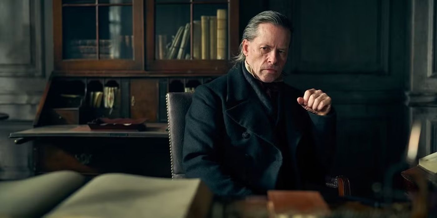 Guy Pearce as Ebenezer Scrooge looks contemplative sitting at a desk in A Christmas Carol.