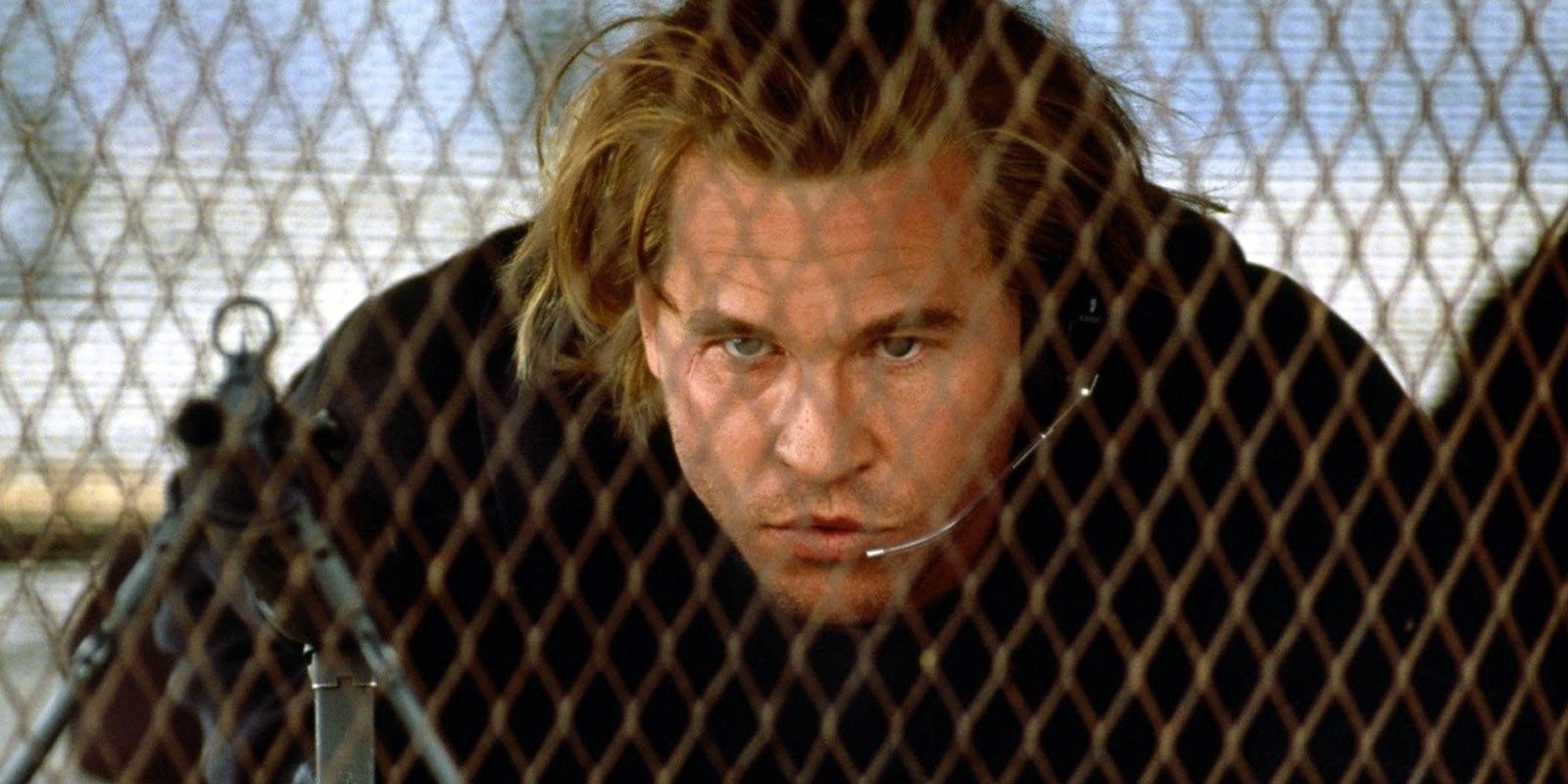 Val Kilmer behind a fence ready to aim a weapon in Heat