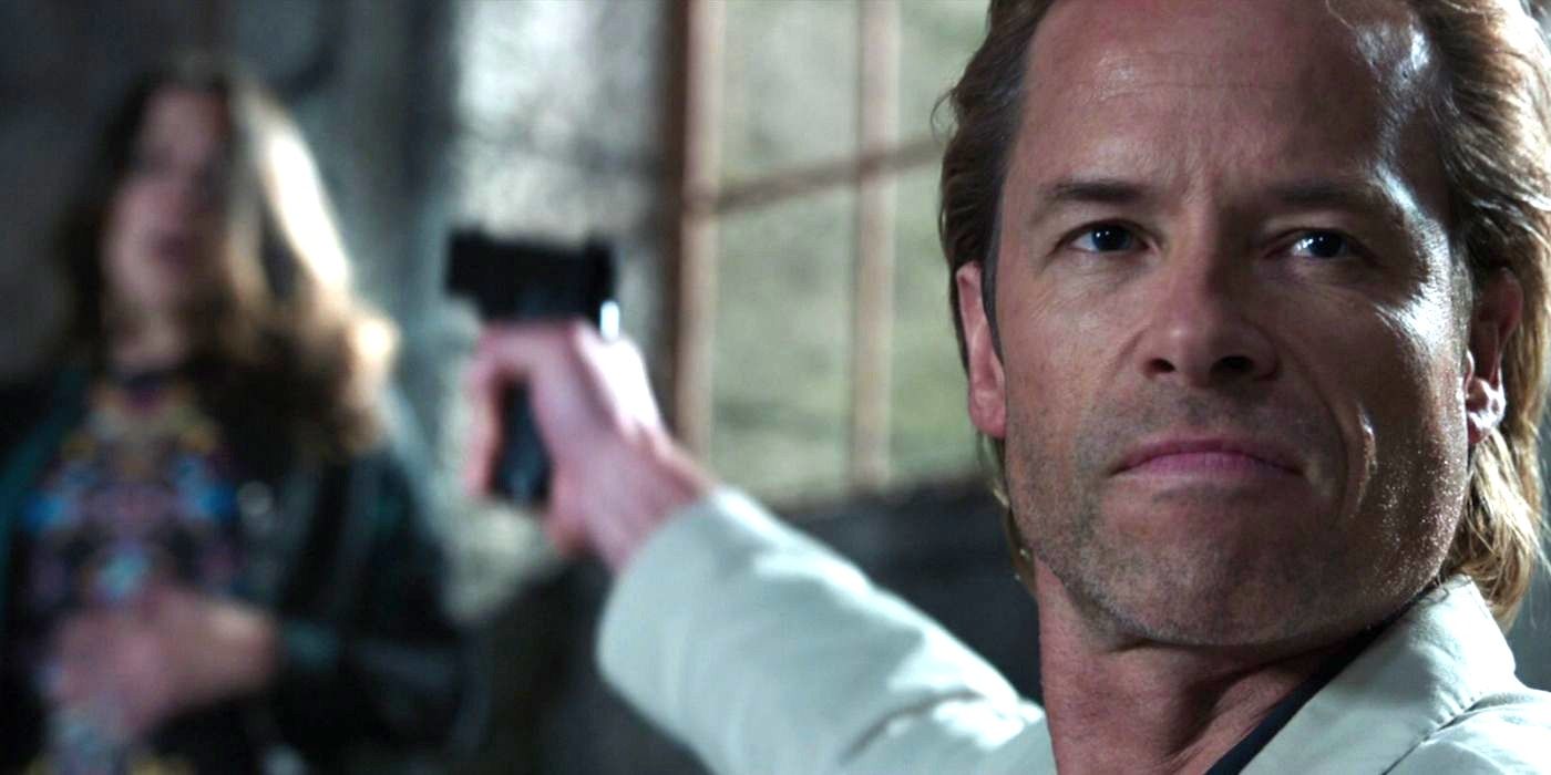 Aldritch Killian (Guy Pearce) in the foreground, looking forward and aiming a gun back at Maya Hansen (Rebecca Hall), who's in the background and blurry, in Iron Man 3