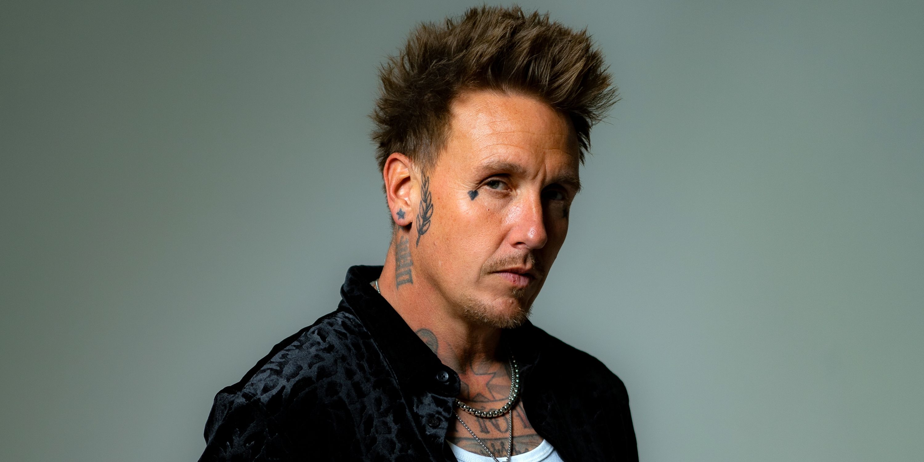 Papa Roach frontman Jacoby Shaddix in slight profile looking down while in a black shirt and white tank top