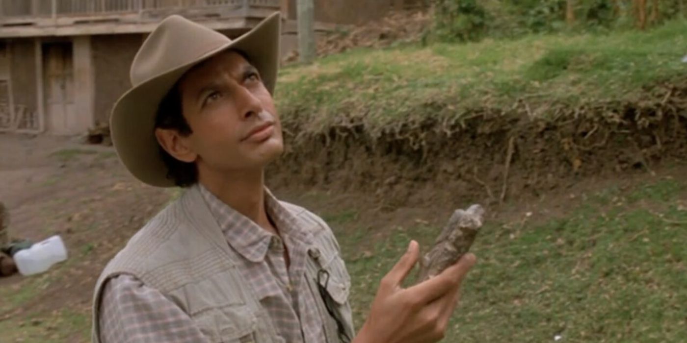 Jeff Goldblum outside a rural jungle village holding an artifact and looking up off camera in Vibes.