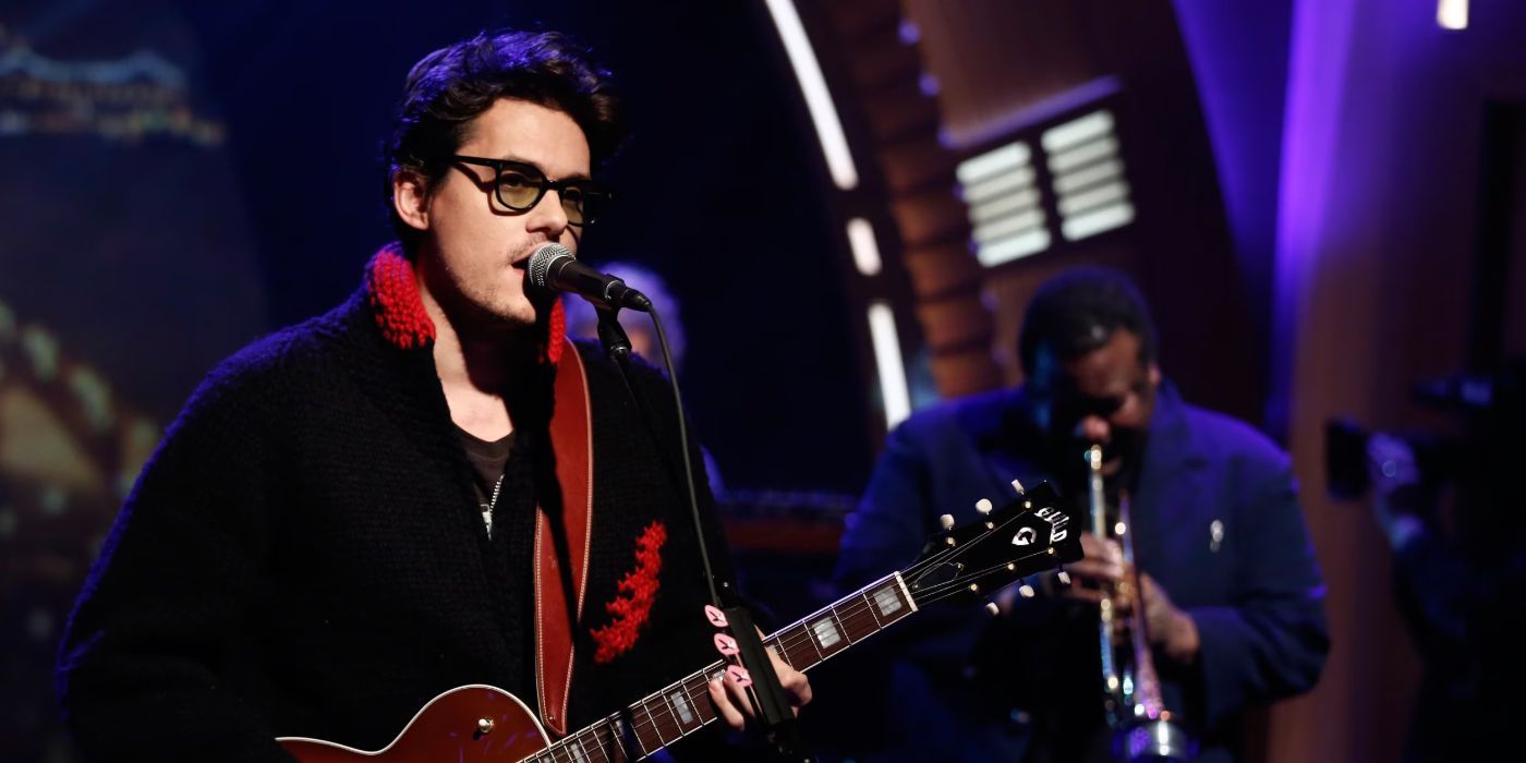 John Mayer plays a guitar and performs on Late Night with Seth Meyers with a band in the background.