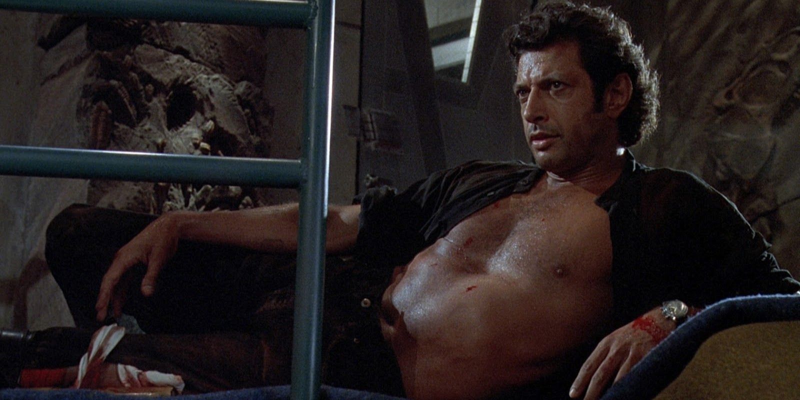 Dr. Ian Malcolm with his shirt open laying down and looking off-camera in Jurassic Park