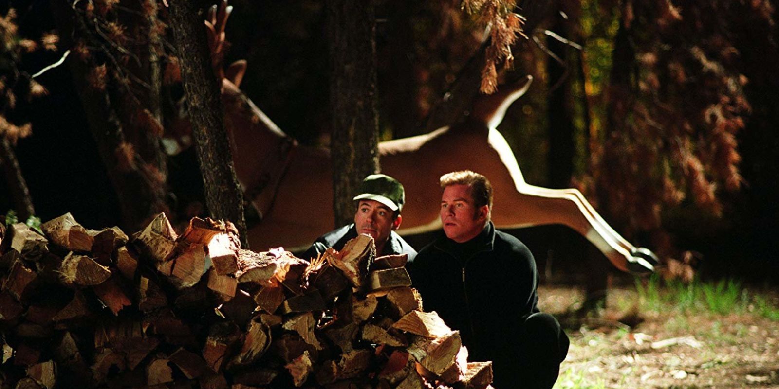 Robert Downey Jr as Harry Lockhart and Val Kilmer as &lsquo;Gay Perry&rsquo; hide behind a stack of fire wood while a large reindeer statue decorates the background