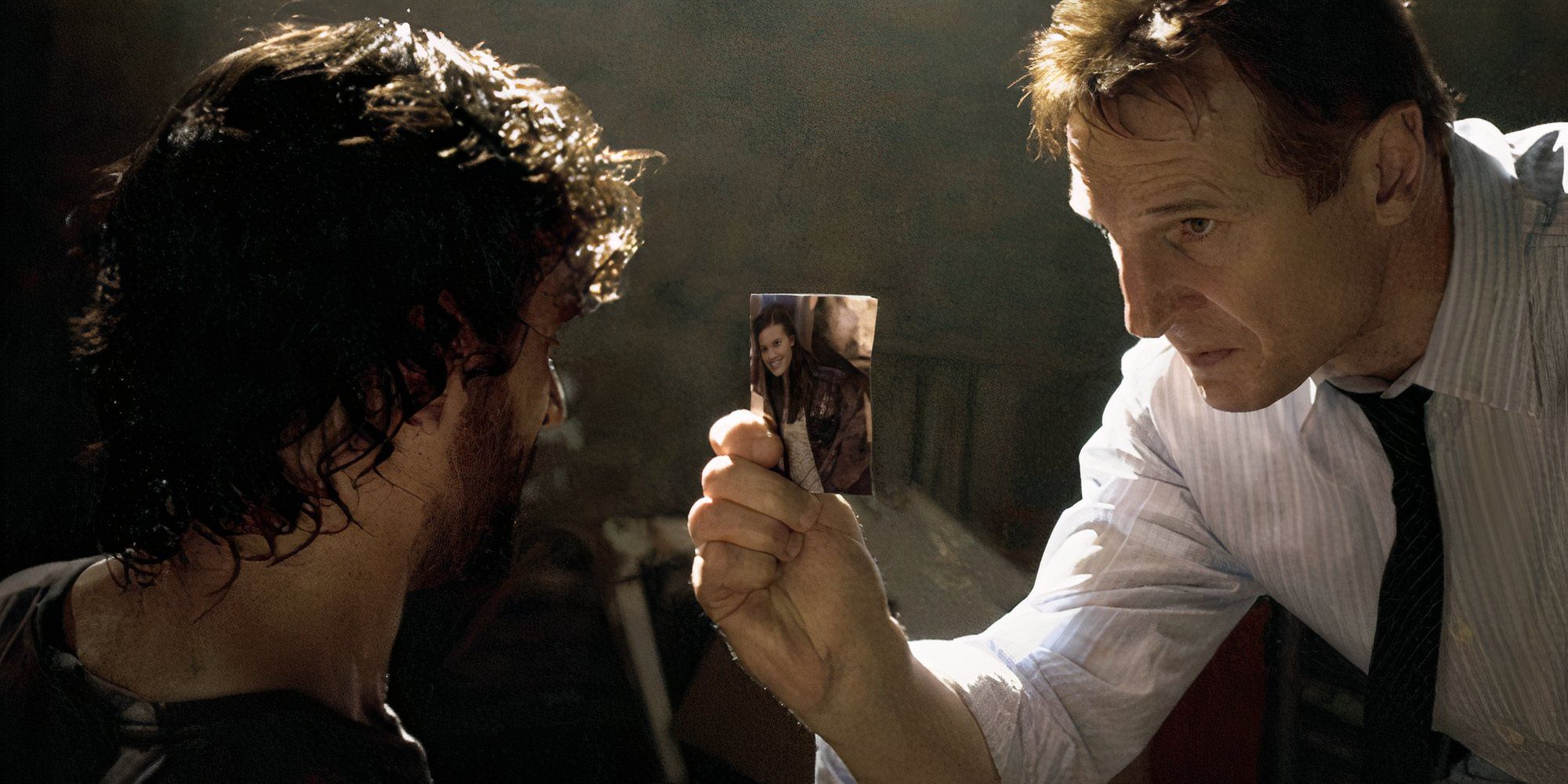 Liam Neeson holding up a photo of his character's daughter and showing it to a man in Taken