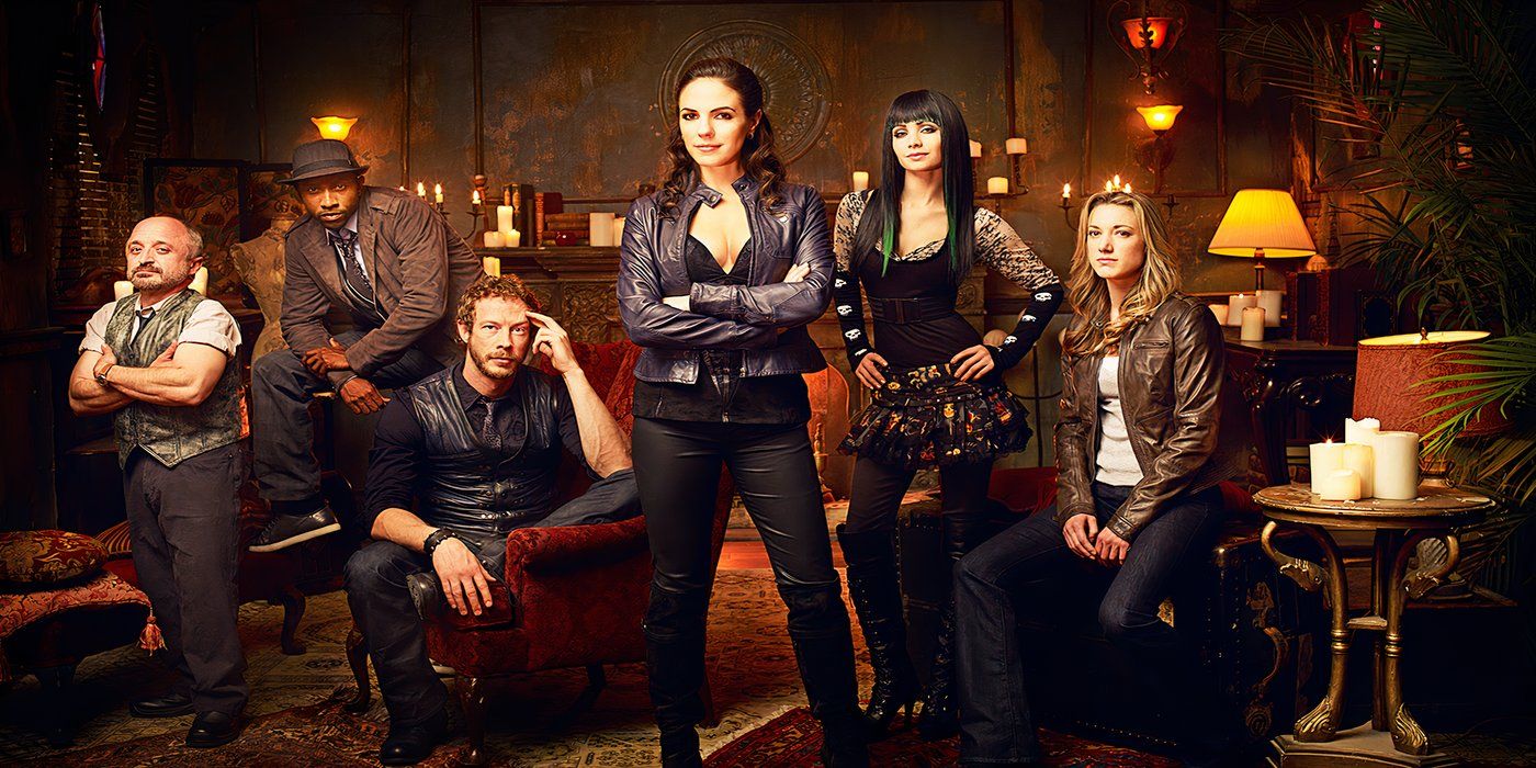 The cast of Lost Girl pose for a promotional photo in a historic and eclectic themed room.