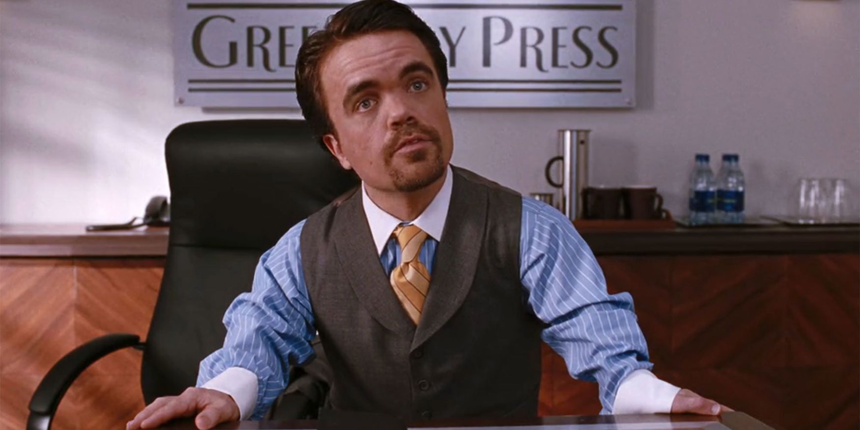 Peter Dinklage as Miles Finch looks annoyed in a conference room with his pitch book in front of him in Elf.