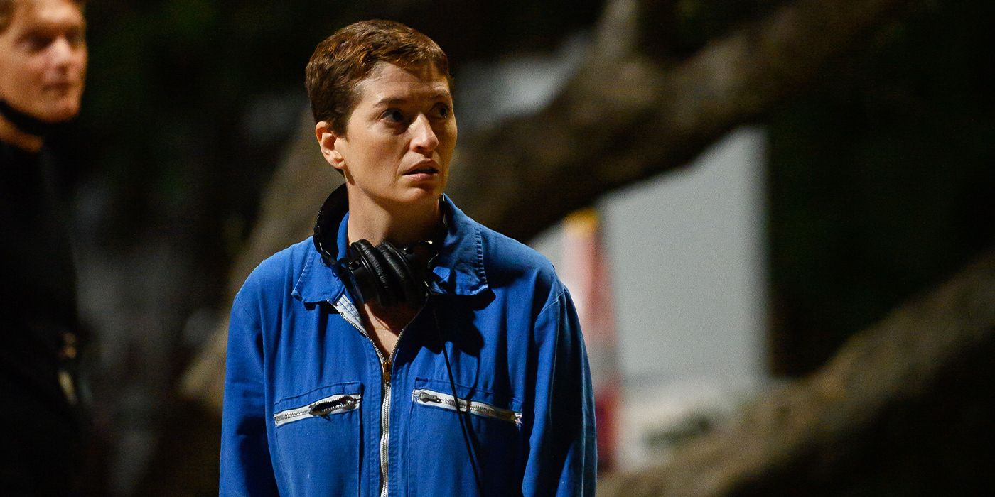 Director Marielle Heller standing on the set of Nightbitch with headphones in a blue jacket