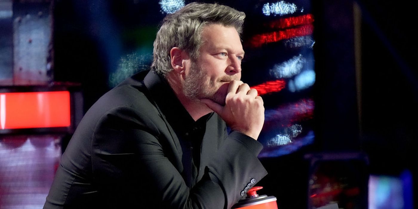 Blake Shelton sits with his chin on his hand in the judges chair 'The Voice' Season 22