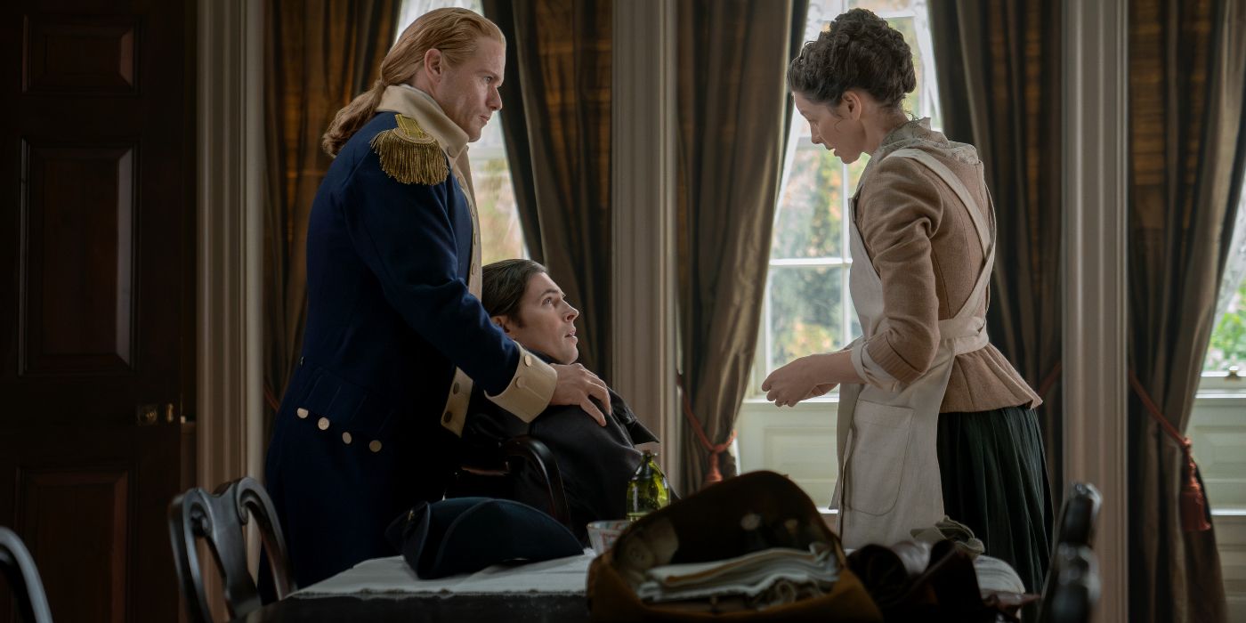 Caitriona Balfe and Sam Heughan standing over a seated David Berry