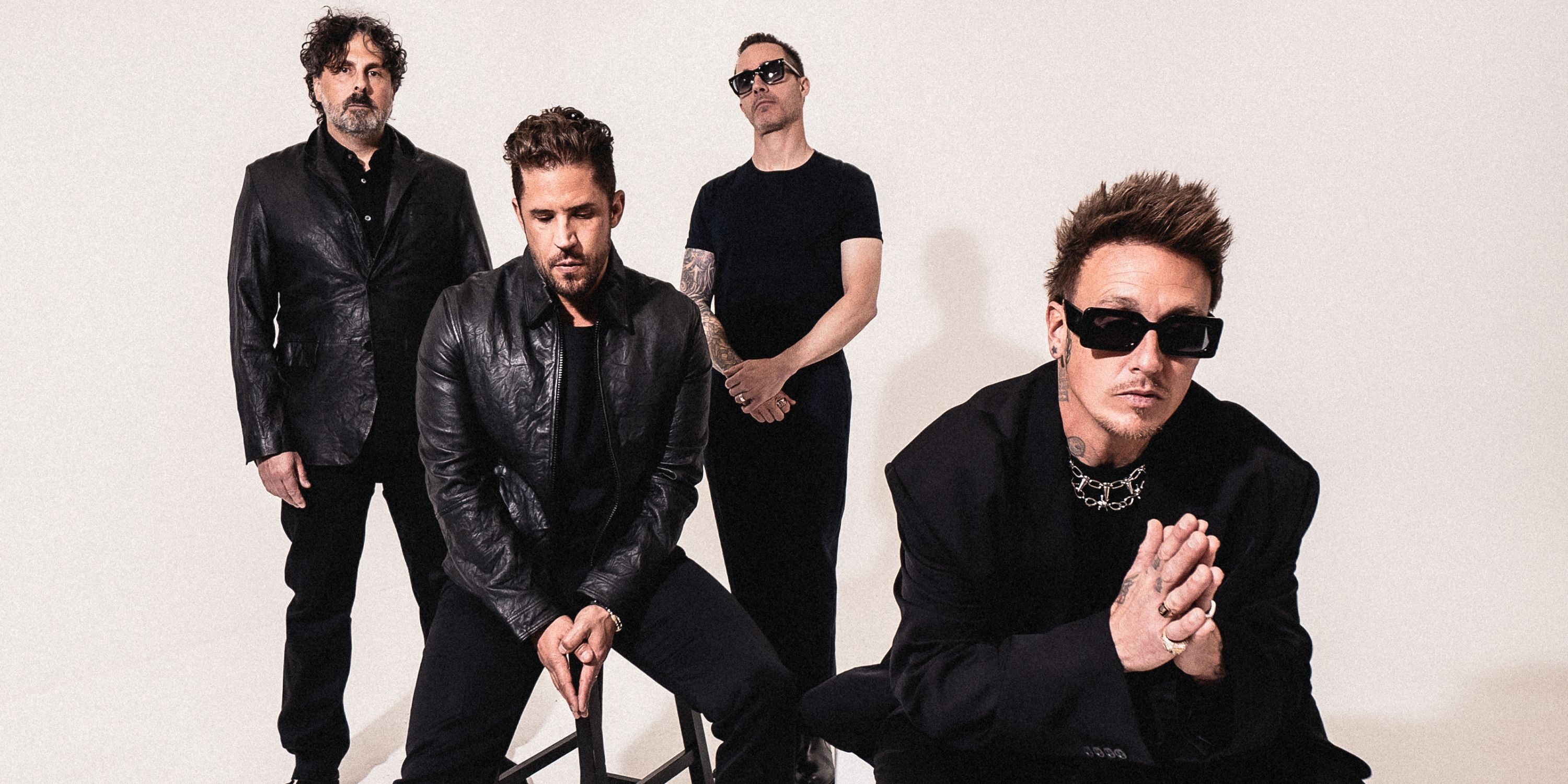 Papa Roach band members in a trio behind frontman Jacoby Shaddix, sitting with prayer hands