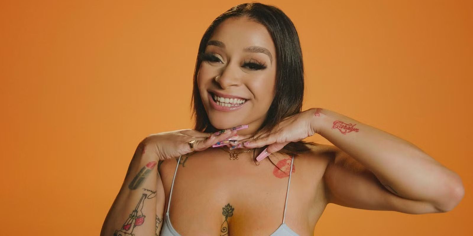 Sam Carmona poses with her hands under her chin in front of an orange background for The Circle.