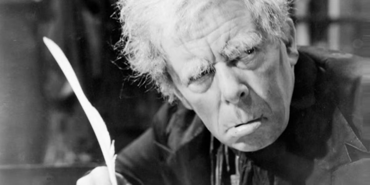 Sir Seymour Hicks as Ebeneezer Scrooge looks grumpy and writes with a quill in Scrooge (1935).