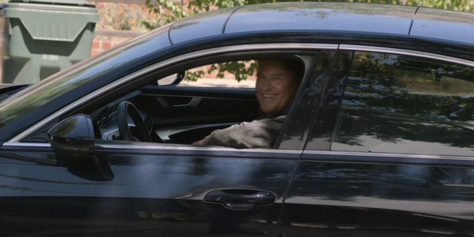 Derek, played by Ted McGinley, smiles as he looks out of his car window in 'Shrinking'.