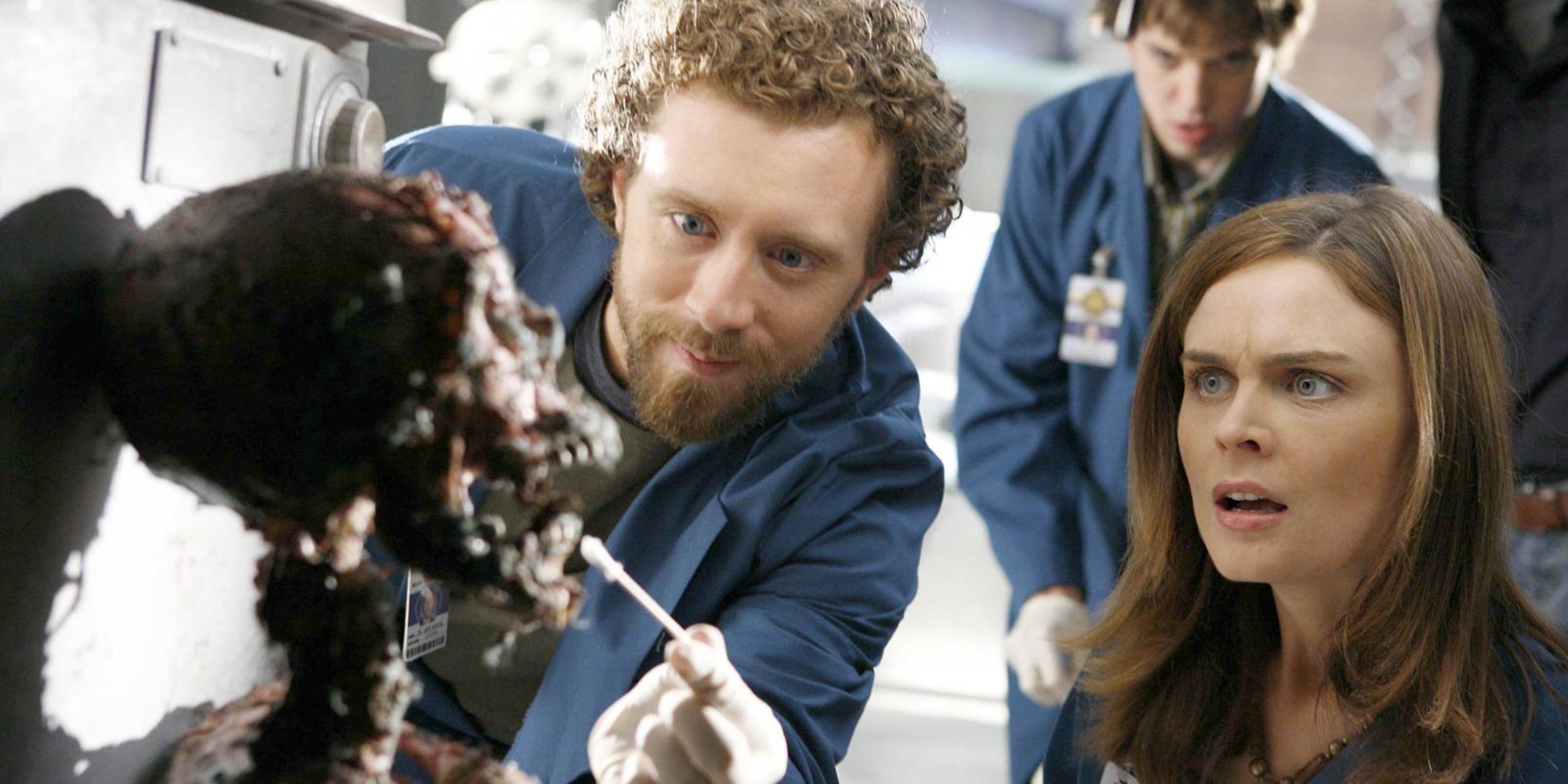 T.J. Thyne standing next to Emily Deschanel while both are looking at a decomposed skeleton in Bones episode The Man in the Fallout Shelter