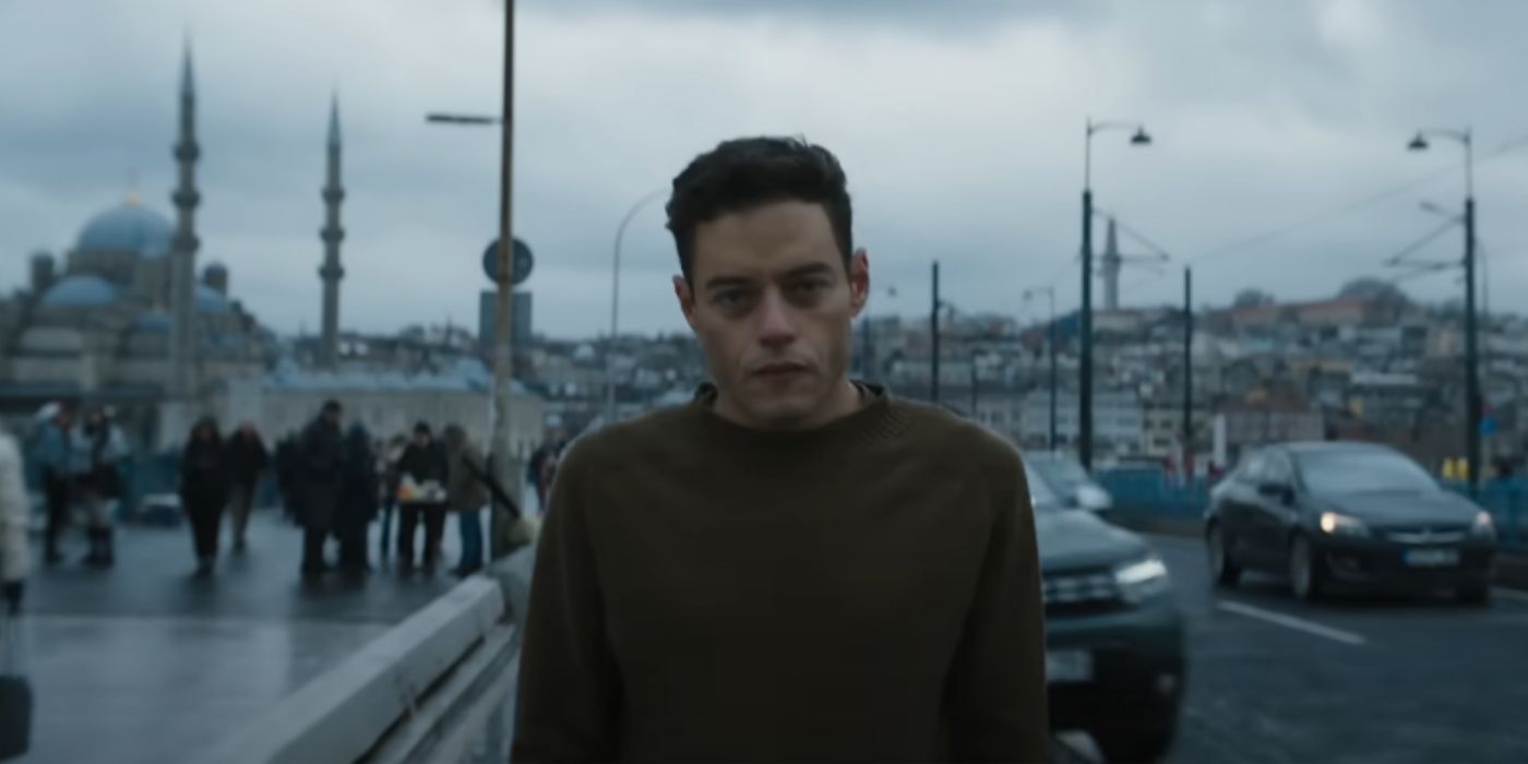 Charles Heller (Rami Malek) walking down the street next to several cars in &lsquo;The Amateur&rsquo;.