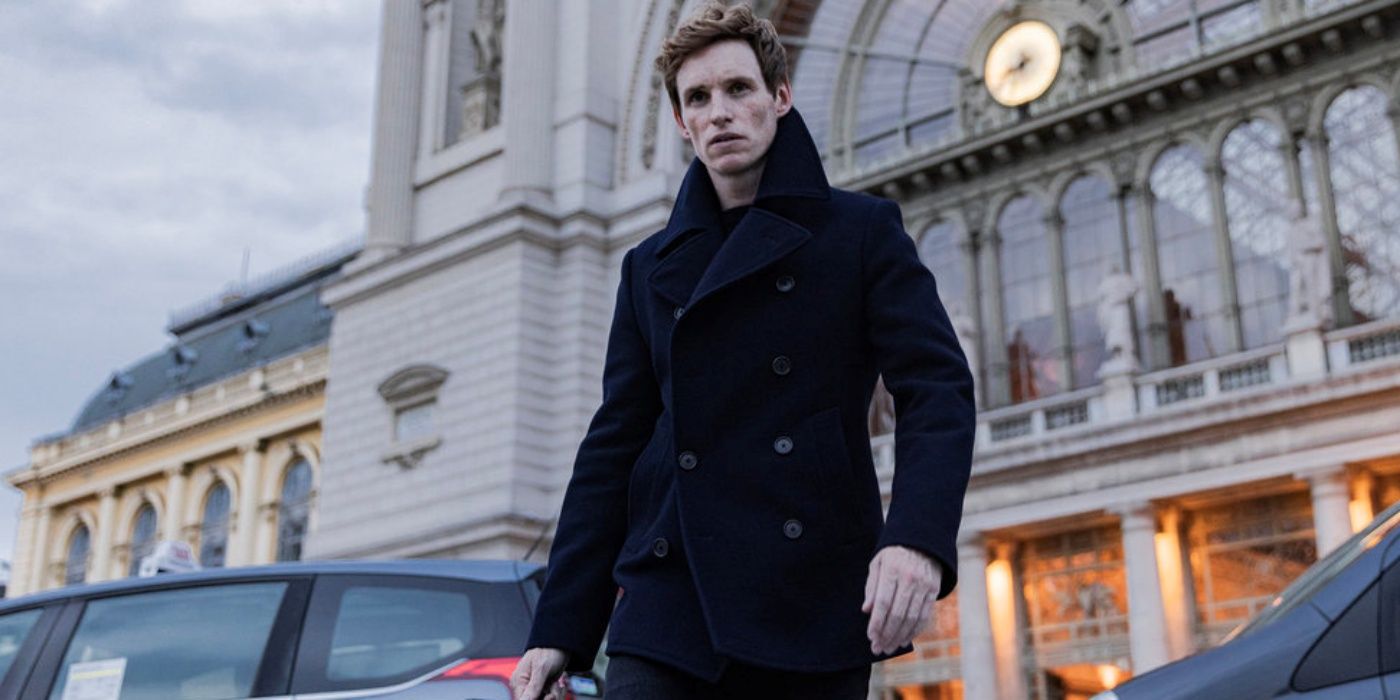 Eddie Redmayne as The Jackal in a pea coat walking across the street outside in The Day of the Jackal