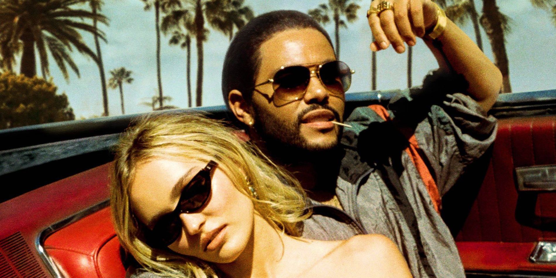 Two people wearing sunglasses ride in a car with palm trees in the background in The Idol, 2023.