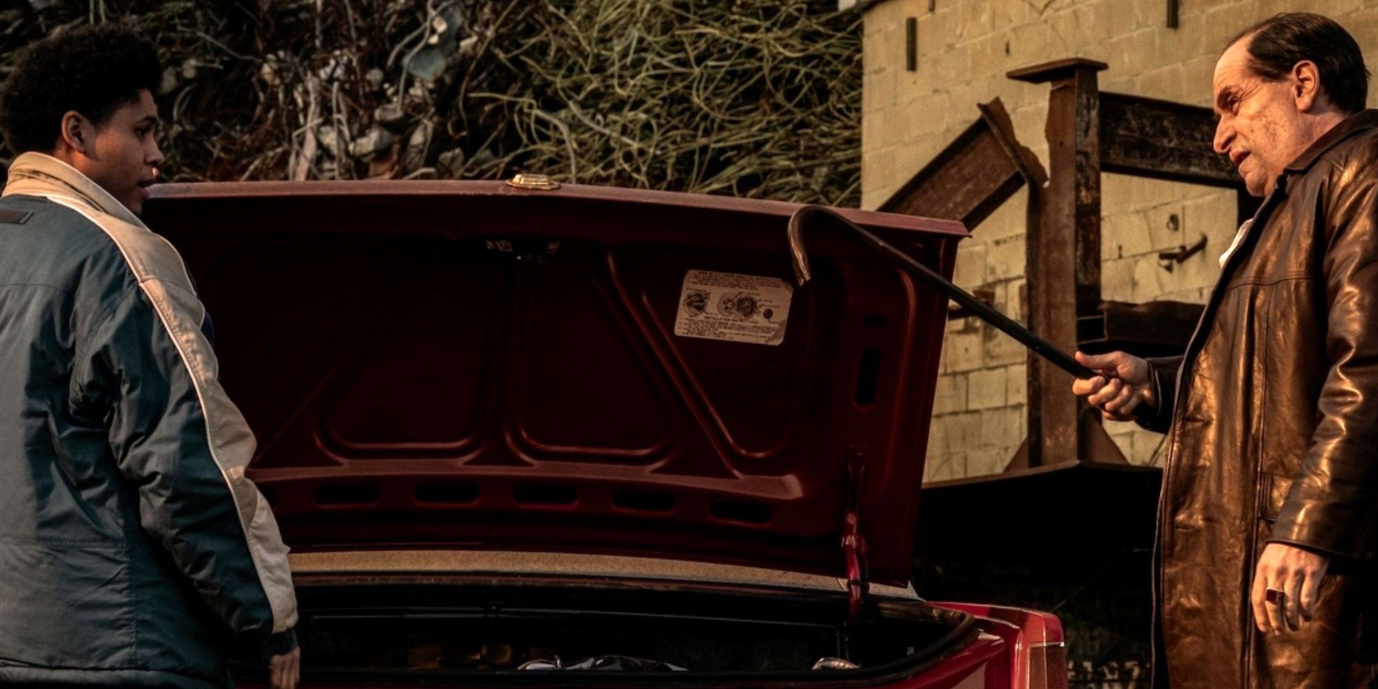 oz-and-vic-stand-on-either-side-of-a-red-car's-open-trunk