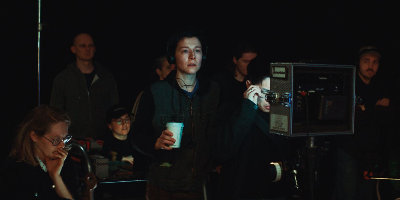 Emma D'Arcy holding a coffee cup and looking at a set in a dark room in The Talent