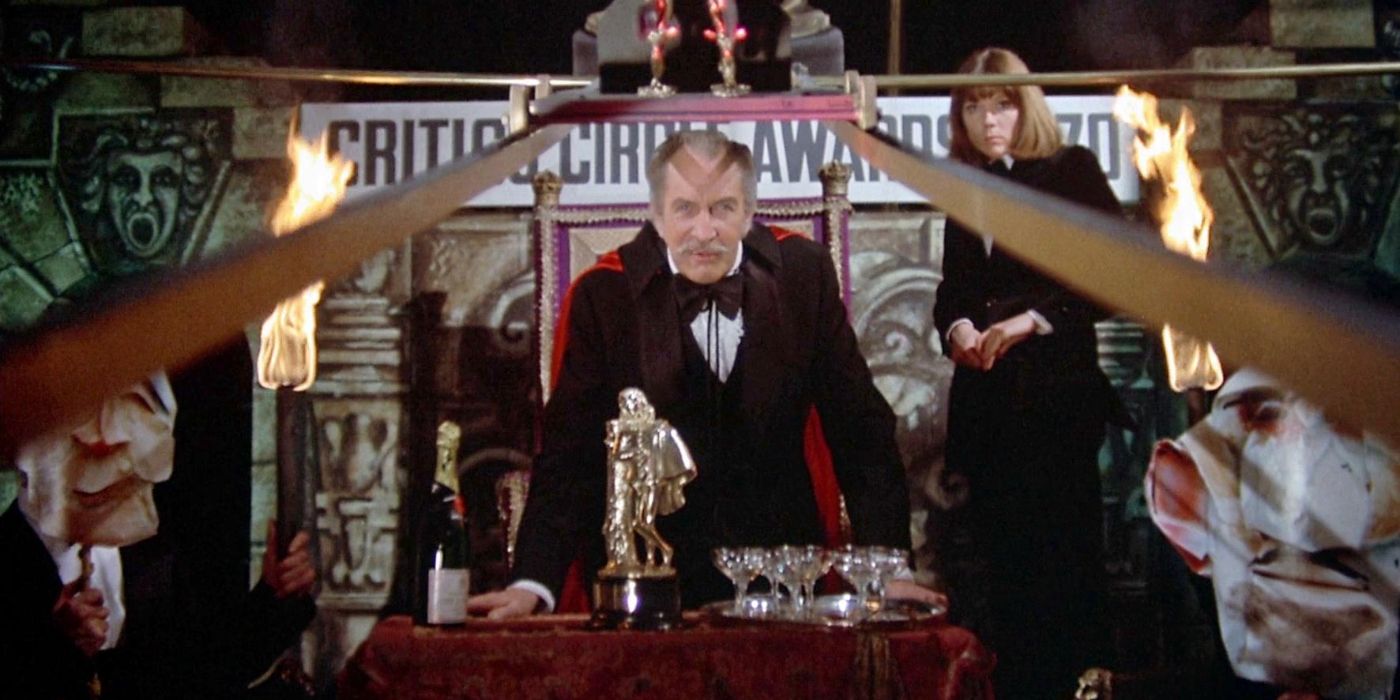 Edward Lionheart (Vincent Prince) wearing a black suit with a red cloak, leaning his hands on a table and staring down the camera with his daughter Edwina (Diana Rigg) standing behind his right shoulder in Theatre of Blood