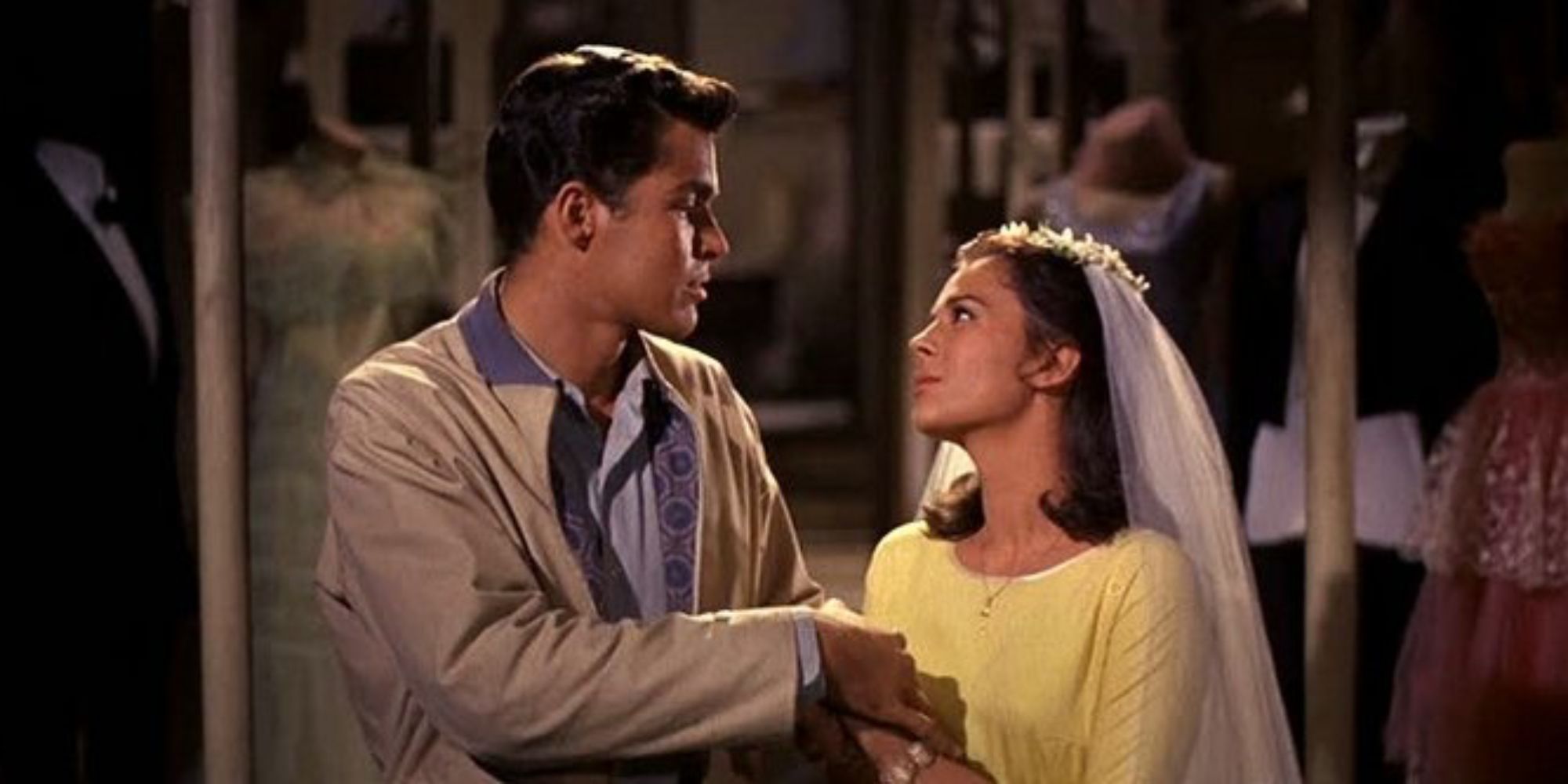 A woman in a wedding veil holds hands with a man and they sing together in West Side Story.