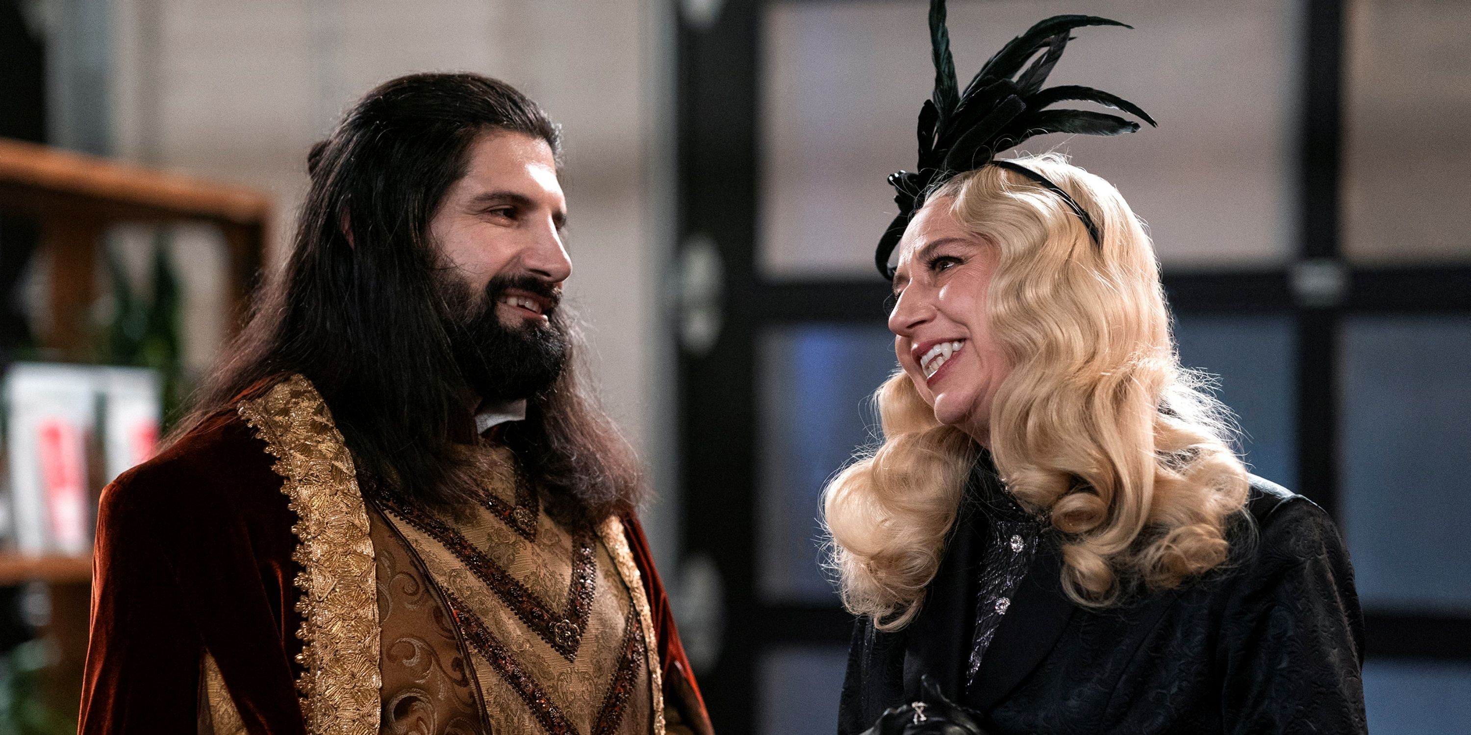 Kayvan Novak as Nandor facing Kristen Schaal as The Guide who's smiling big in What We Do in the Shadows