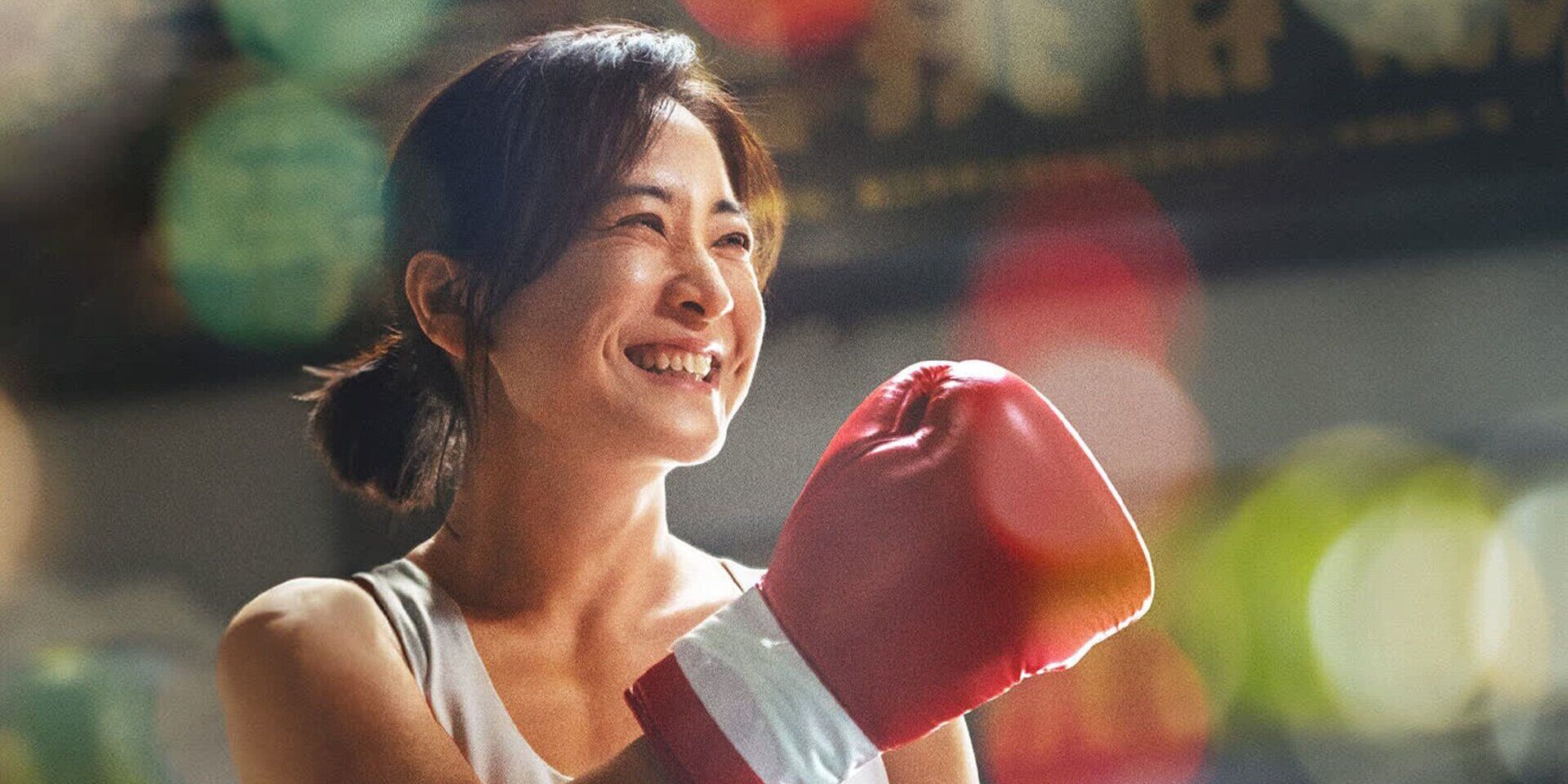 A Chinese woman smiling while raising her hand with a boxing glove on it in 'Yolo' (2024)