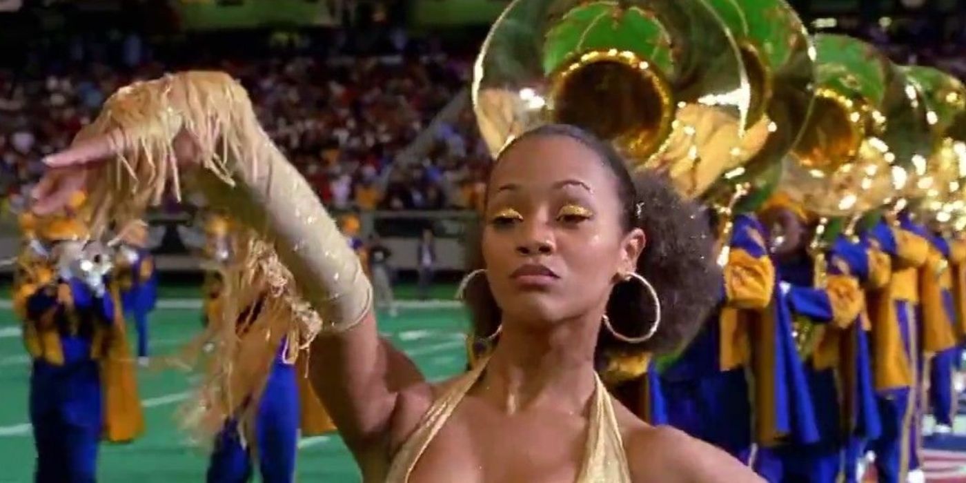 Zoe Saldaña dances in a gold outfit on a football field with a marching band in Drumline.