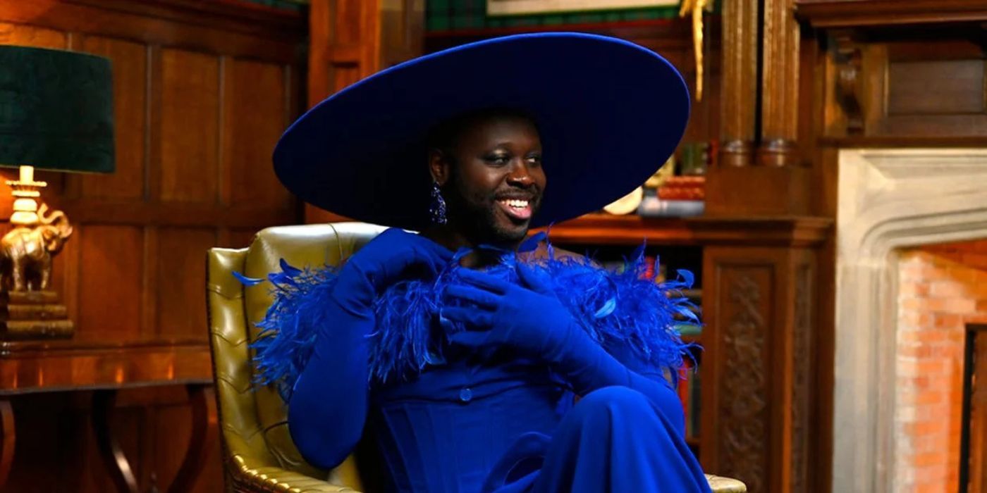 Bob the Drag Queen wears a blue feathered outfit and large hat and sits in a fancy chair in The Traitors.