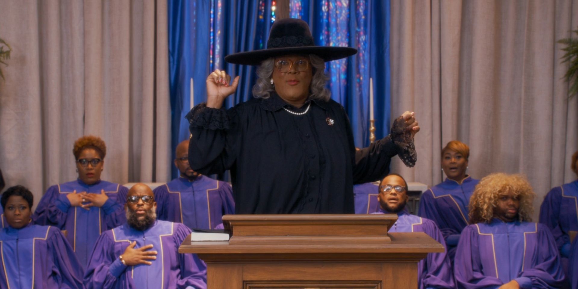 Madea, played by Tyler Perry, stands behind a podium in front of a church choir in 'A Madea Family Funeral'.