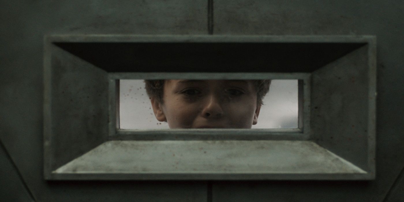 Cameron Bell peers through a narrow window and looks worried in Silo.