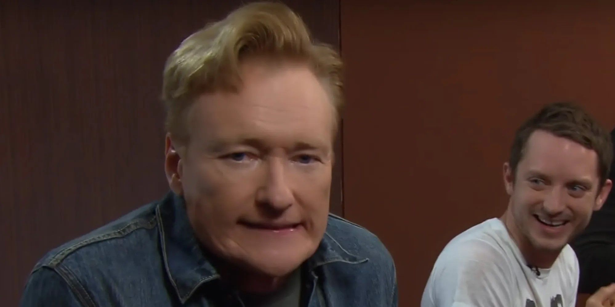 Conan O'Brien grimaces at the camera as Elijah Wood laughs in the background for Clueless Gamer on Conan.