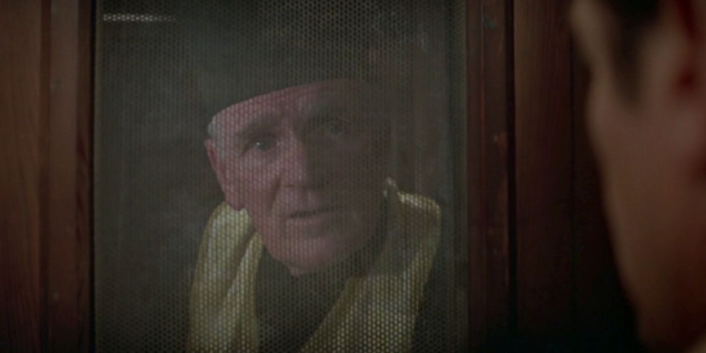 Desmond Llewelyn as Q masked in a priest's garment, talking to Bond through the confessional booth