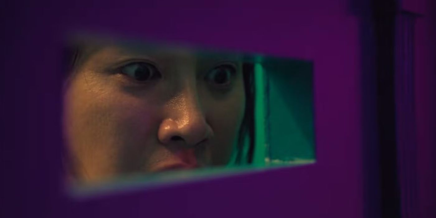 Hyun-ji stares out the gap of the locked door as she watches Young-mi get shot down in Squid Game, Mingle.
