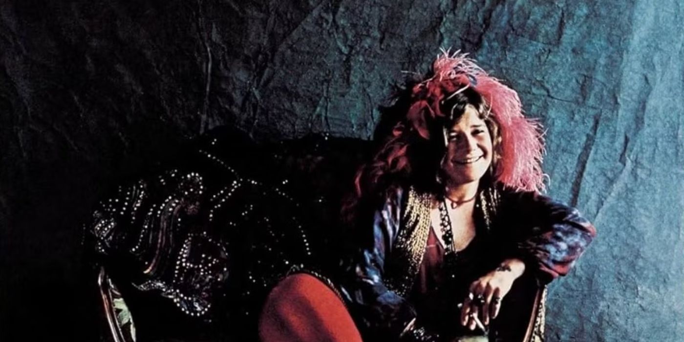 Janis Joplin with a pink headdress reclines on a couch and smiles on the album cover for Pearl (1971).