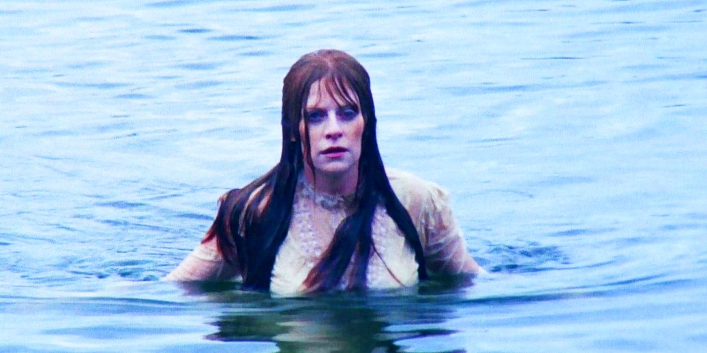 A pale, gaunt looking woman in a white nightdress submerged up to her chest in a lake.