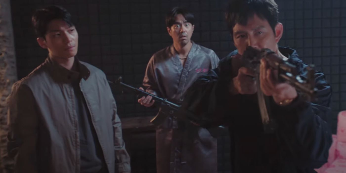 Gi-hun holding an automatic gun and pointing it at something off-screen in front of him, while Jun-ho looks at him and Woo-seok looks shocked