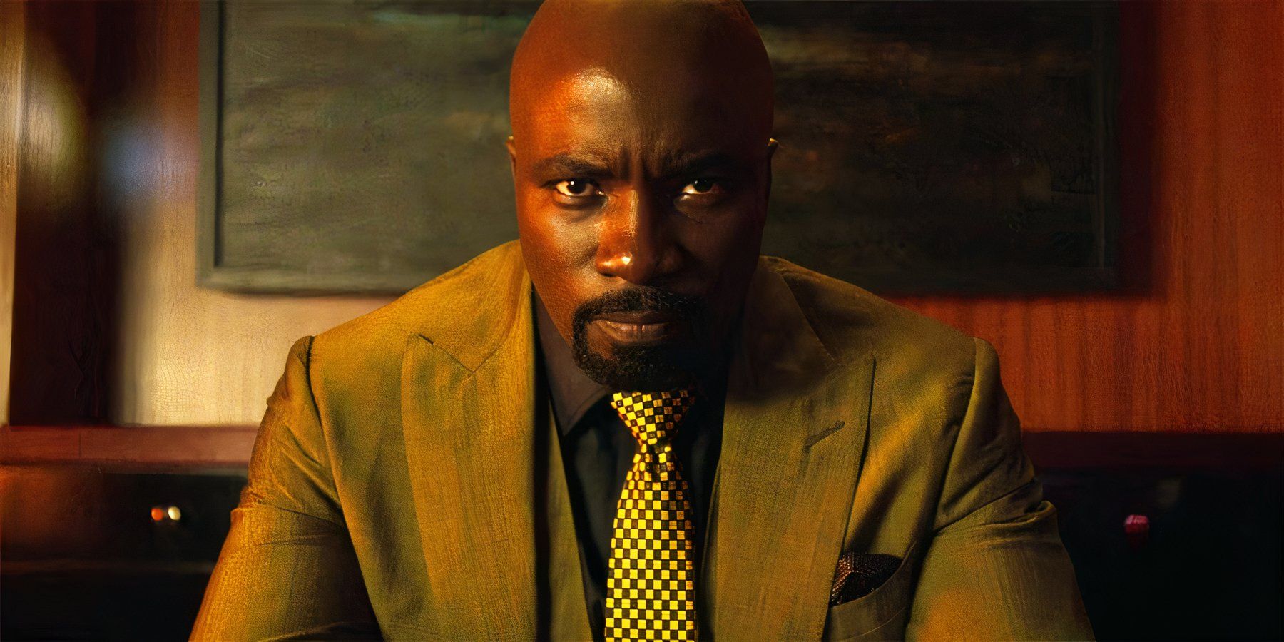 Mike Colter as Luke Cage wearing a suit and tie sits in an office with a serious and stern stare in Luke Cage.