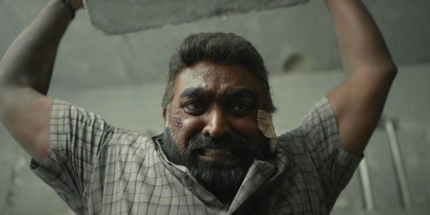 Vijay Sethupathi as Maharaja with a teary eyed look on his face as he lifts a concrete block above his head in &lsquo;Maharaja&rsquo; (2024)